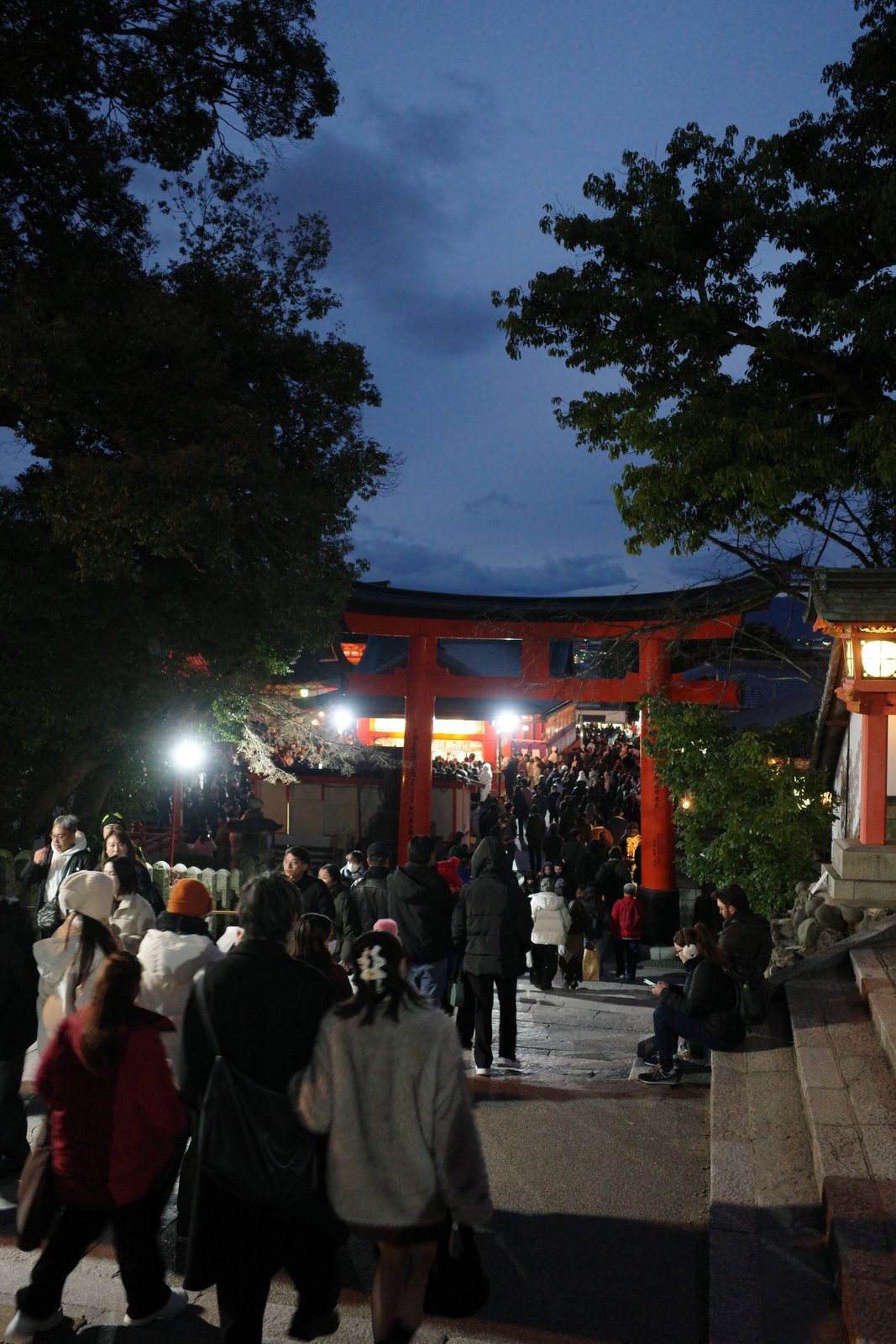 crowds at a vermilion torii gate at dusk